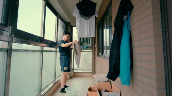 A young man is hanging washed clothes to dry in an enclosed brick and glass wall balcony.