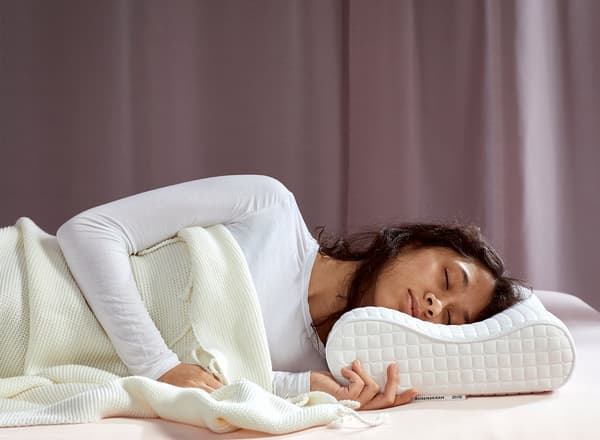 A young woman, laying on her side, is sleeping deeply on IKEA ROSENSKÄRM ergonomic pillow.