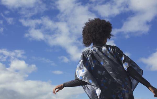 A young woman outdoors wearing a patterned black, blue and white kaftan from the IKEA ANNANSTANS collection.