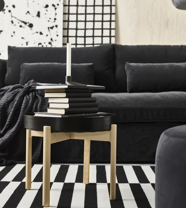 A YPPERLIG black topped coffee table with four birch legs, stacked with black books and a YPPERLIG black candleholder.