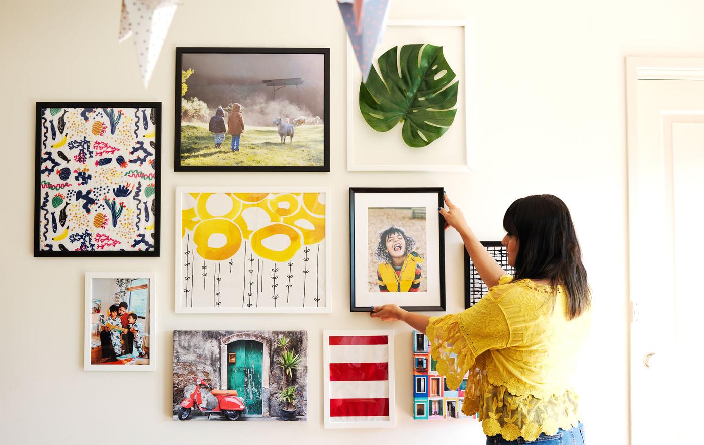 Abeer placing a framed photograph on a gallery wall of pictures and artwork.