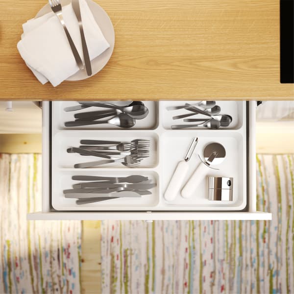 Åben køkkenskuffe set fra oven med STÖDJA bestikindsats, hvor bestik og køkkenredskaber er organiserede.