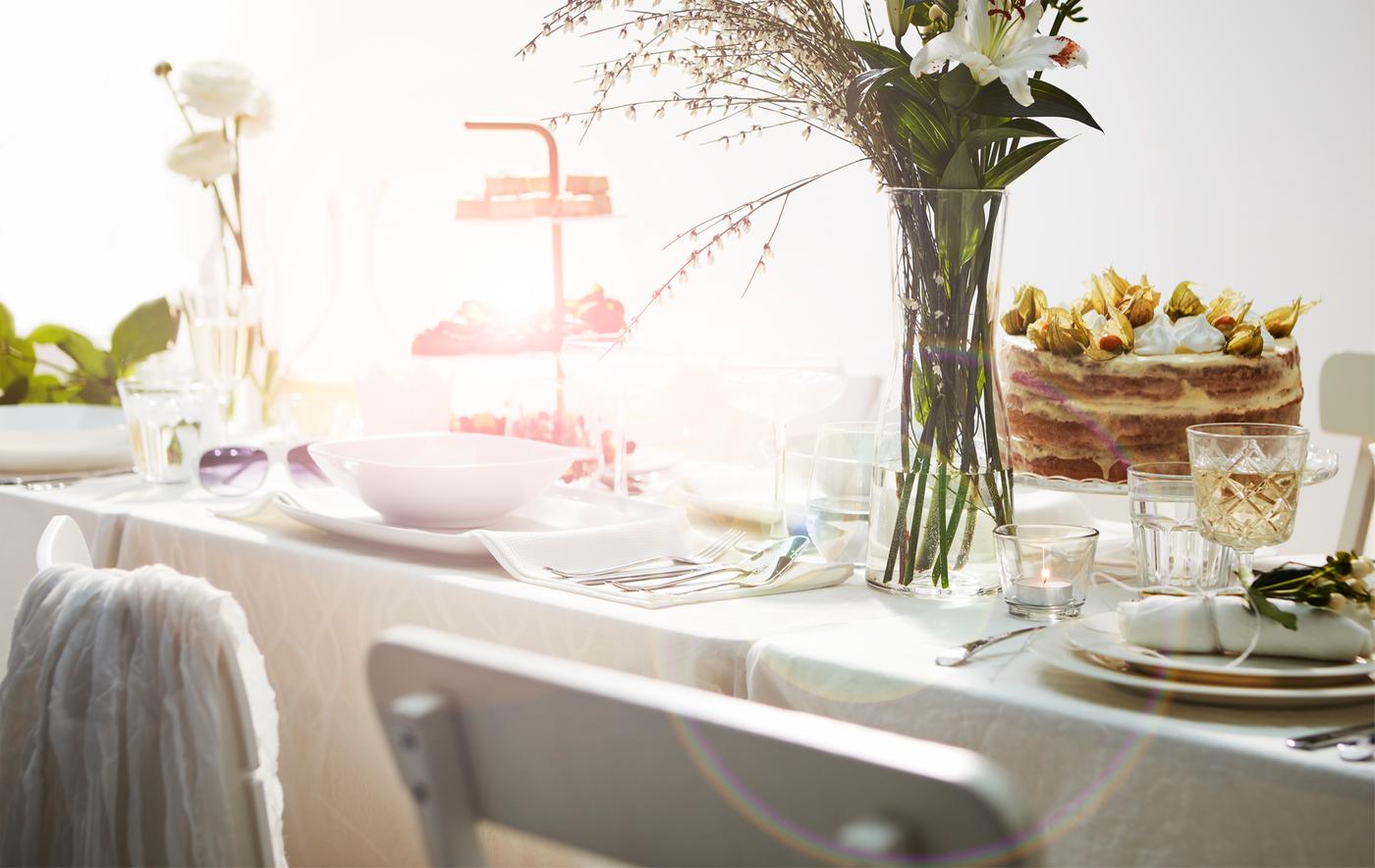 Abschnitt eines romantisch in Weiß gedeckten Tisches mit FRAMTRÄDA Weingläsern und Blumen.