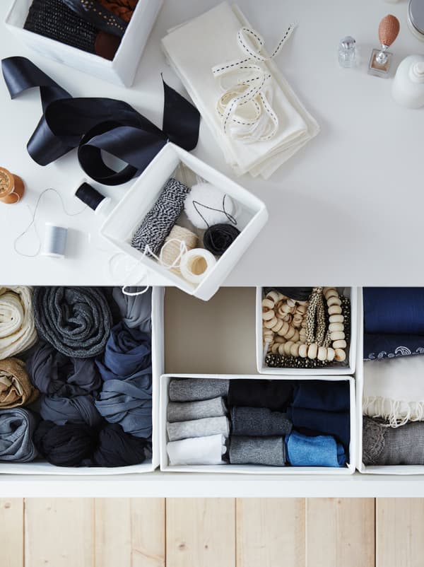 Accessoires de couture posés sur une commode. Un tiroir ouvert révèle des vêtements bien rangés dans les boîtes SKUBB.