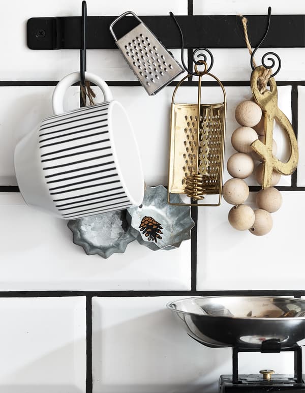 Accessoires de cuisine accrochés à une barre noire fixée sur des carreaux blancs.