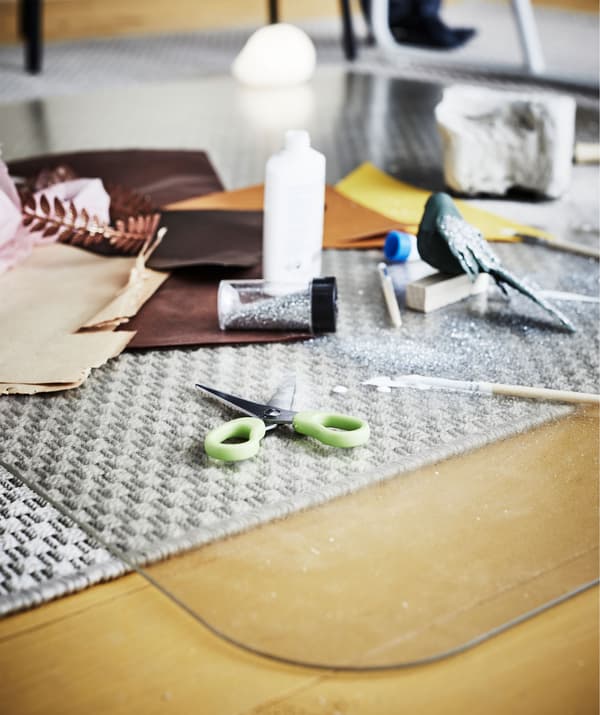 Accessoires de dessin, de peinture et de papier découpé répandus sur une protection pour sol qui met le tapis sous-jacent à l’abri du danger.