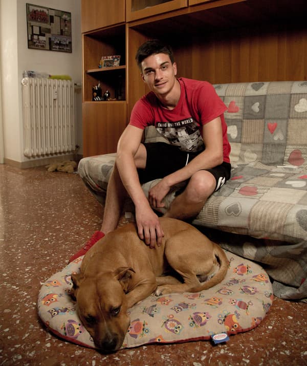 Alessandro sits on a sofa and a dog lies on a dog bed in front of him.