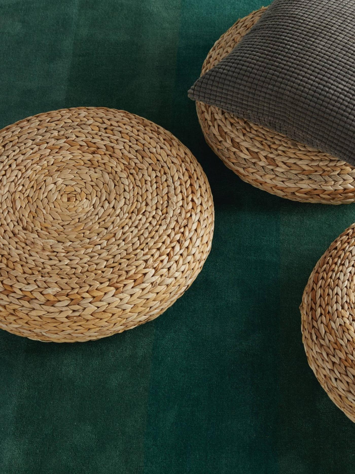 ALSEDA rattan stools placed over green carpet. A cushion over a rattan stool.