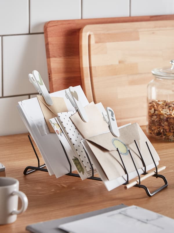 Amid scattered kitchen accessories, a RINNIG plate holder lies horizontally, repurposed to hold envelopes and papers.