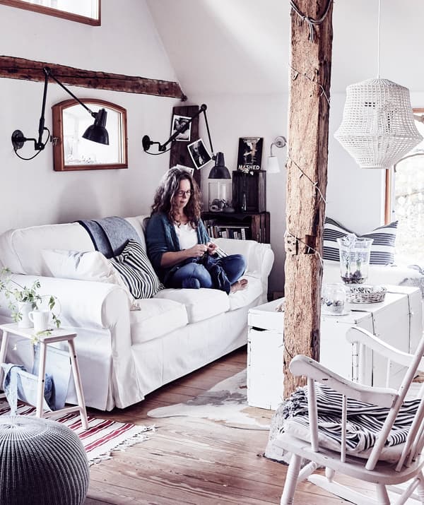 امرأة تجلس على صوفا بيضاء في غرفة معيشة مع عوارض خشبية وألواح أرضية.