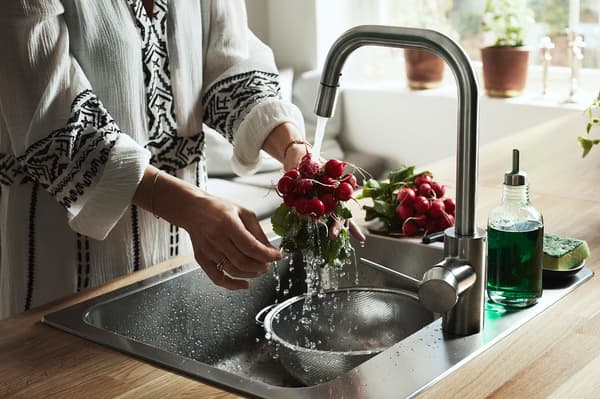 امرأة تقف بجانب حوض المغسلة تشطف كمية من الفجل باستخدام حنفية المطبخ ÄLMAREN.