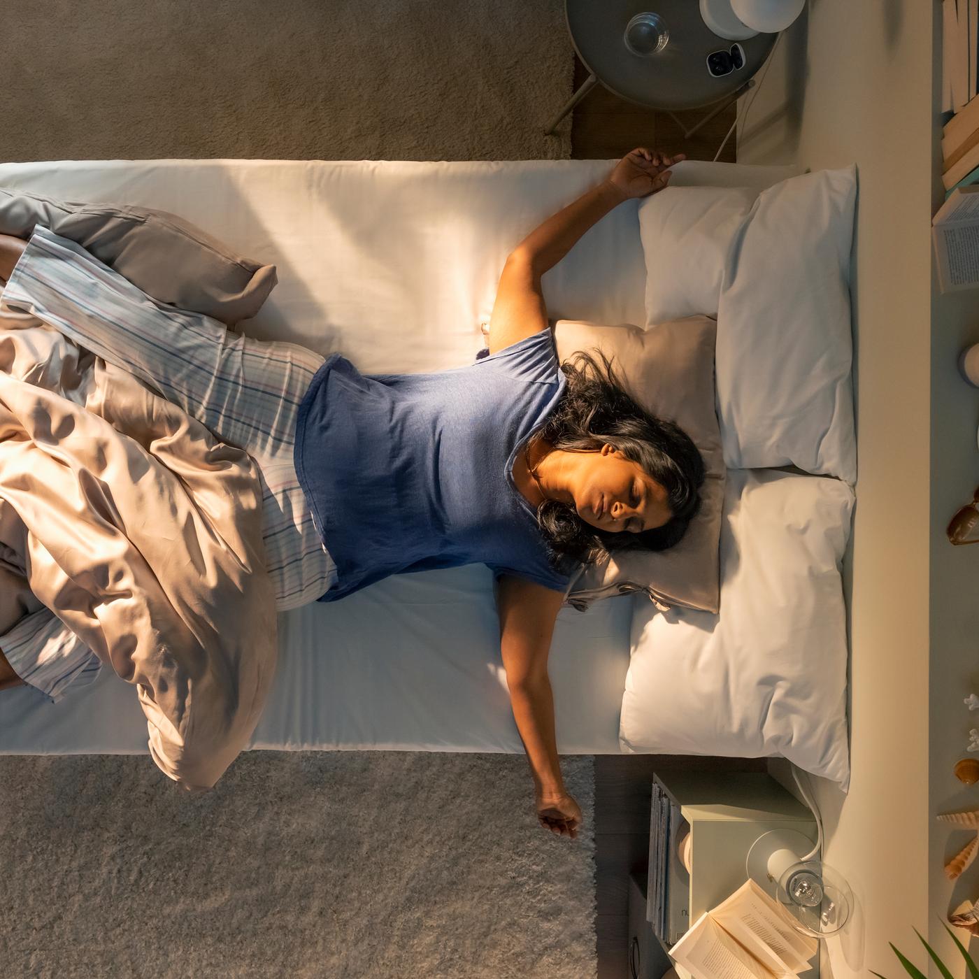 An aerial view of a person asleep on their back on a bed, partially covered by a beige KRITSUGA duvet cover with pillowcase.