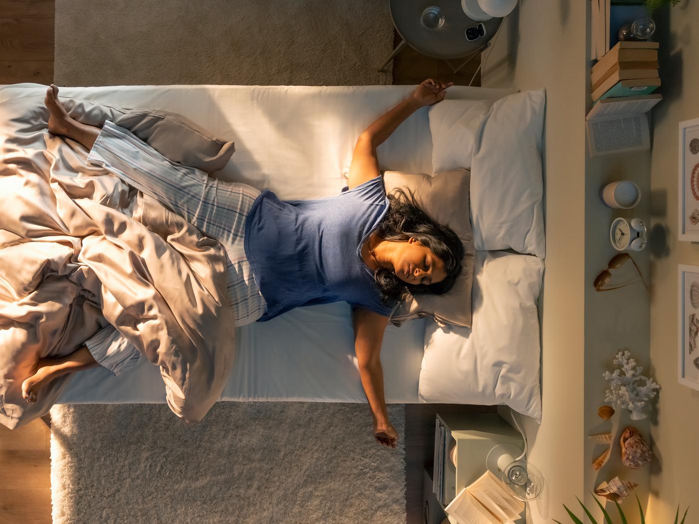 An aerial view of a person asleep on their back on a bed, partially covered by a beige KRITSUGA duvet cover with pillowcase.
