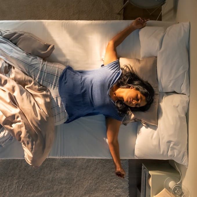 An aerial view of a person asleep on their back on a bed, partially covered by a beige KRITSUGA duvet cover with pillowcase.