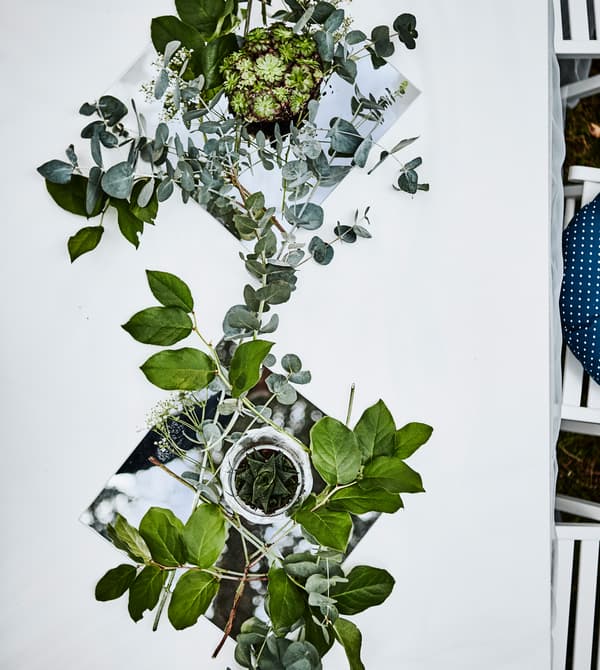 An aerial view of a set table with a white tablecloth and a table runner centrepiece made from mirrors, greenery and small succulents