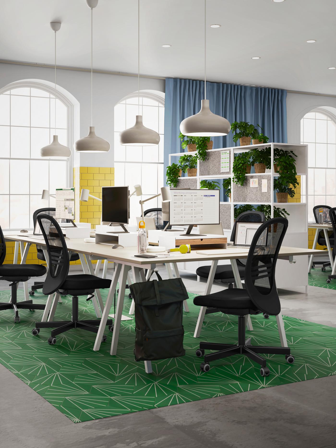 An airy office with several black FLINTAN office chairs around a cluster of TROTTEN desks, forming a large, shared workspace.