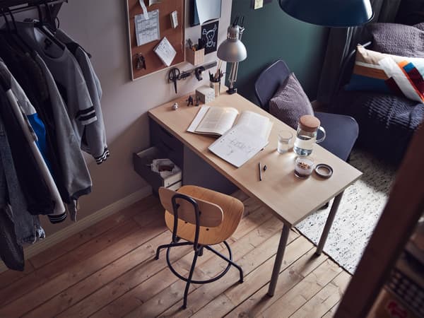 An angled room view with a desk and chair in the foreground and a day-bed in the background.