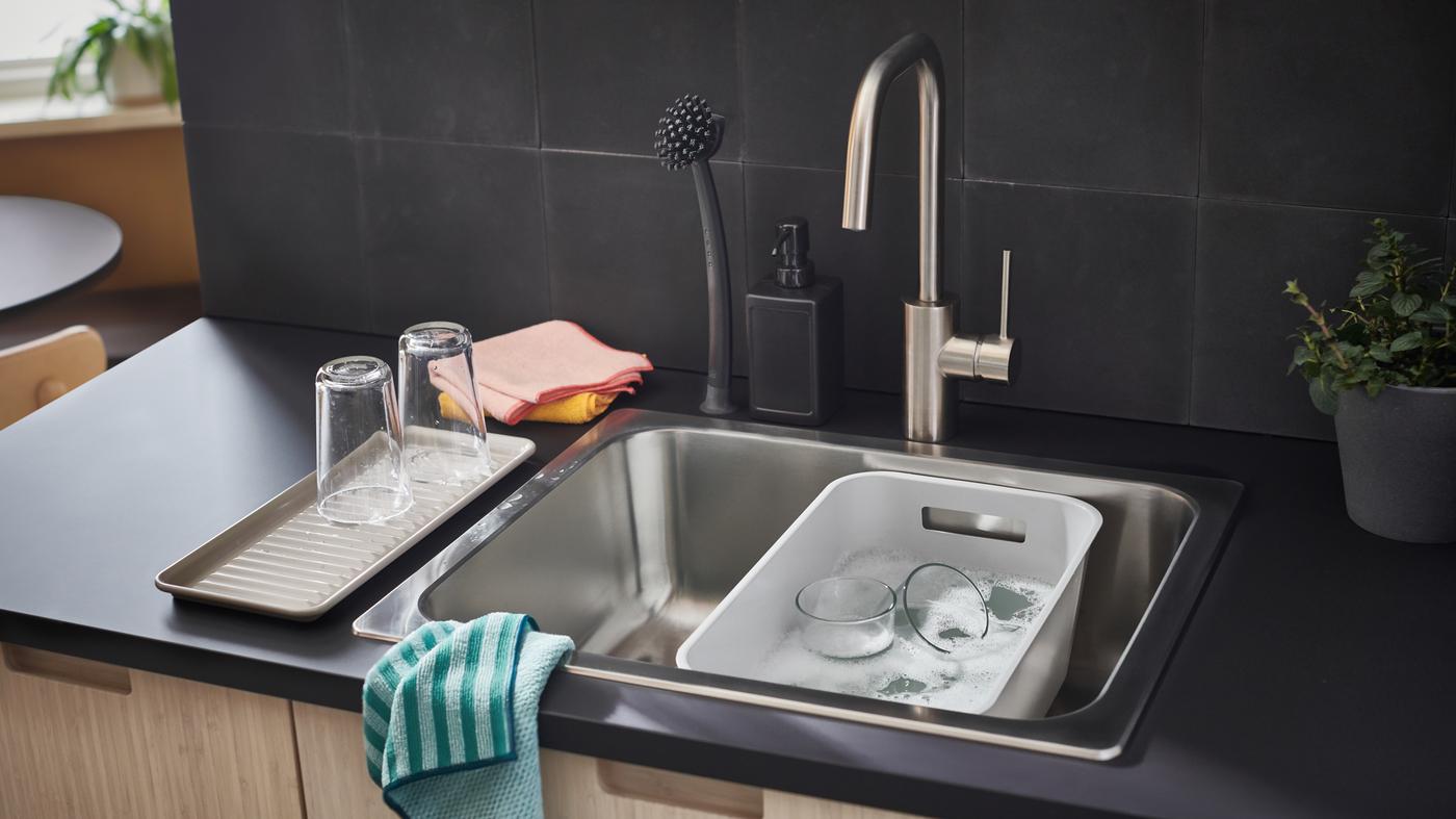 An anthracite EKBACKEN countertop with a sink holding a gray GRUNDVATTNET washing bowl, microfiber cloths and accessories.