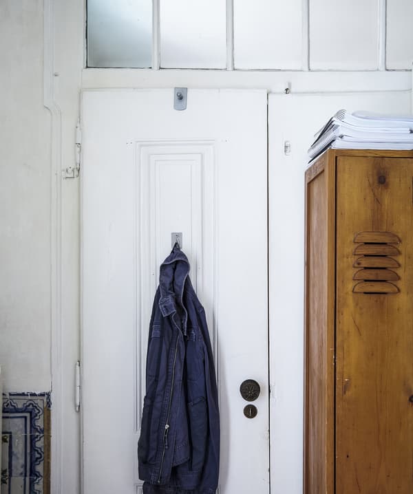 An antique wooden locker cabinet next to a white door with a shirt hanging from it.
