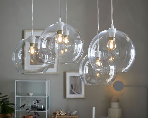 An arrangement of five IKEA JAKOBSBYN circular clear glass pendant lampshades that expose the bulb inside.