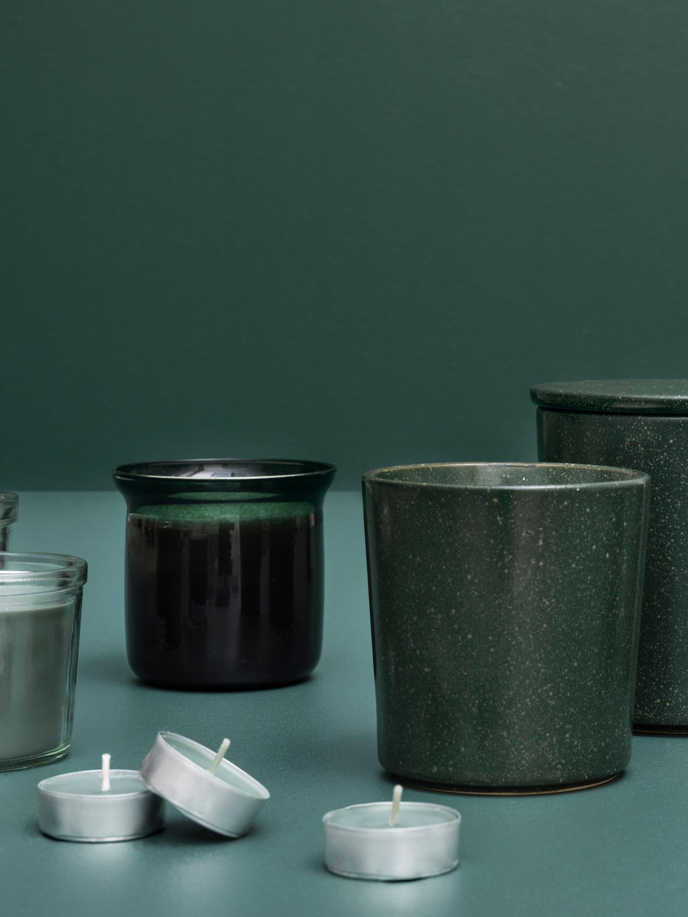 An artistic display of several AVMÅLA crisp mint scented candles in different containers against a dark green background.