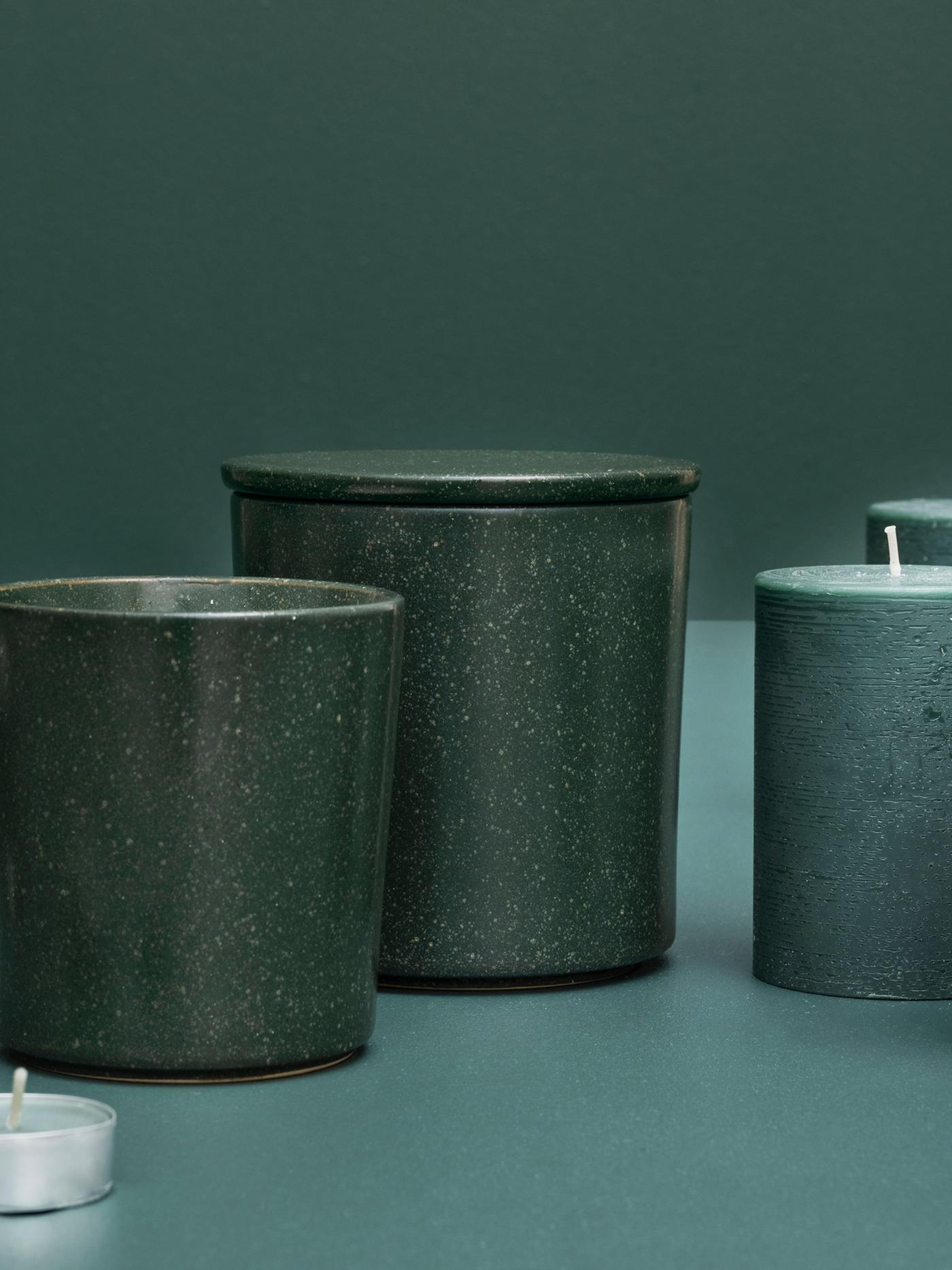 An artistic display of several AVMÅLA crisp mint scented candles in different containers against a dark green background.
