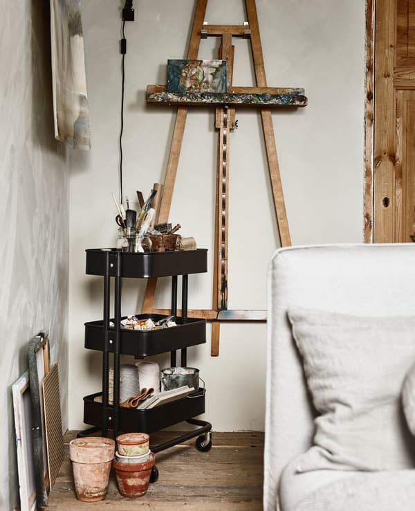 An easel hung on a wall, with a trolley next to it holding art supplies.