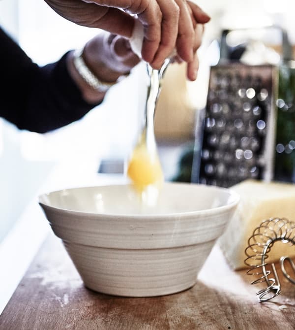 An egg is being broken into a white bowl.