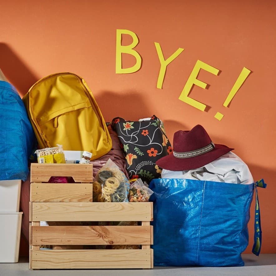 An einer orangenen Wand stehen blaue Taschen von IKEA und eine Holzkiste dazwischen.