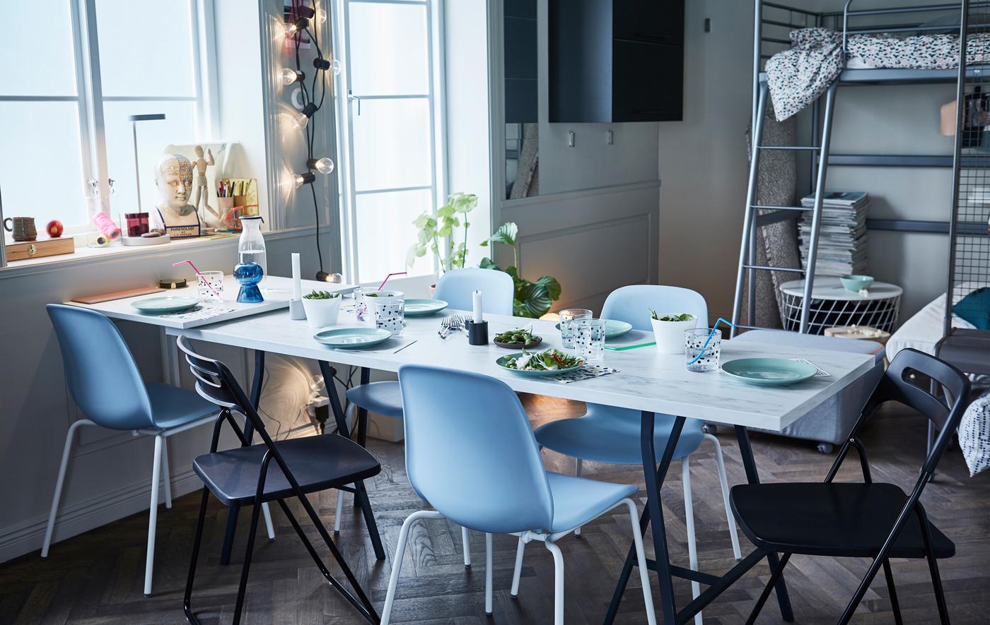 An EKBACKEN work top with white marble effect used as a pop-up table top surrounded by stackable and foldable chairs.