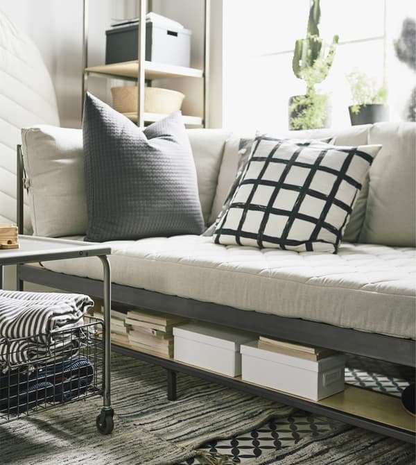 An EKEBOL sofa in beige and steel that has shelves for storage underneath and behind.