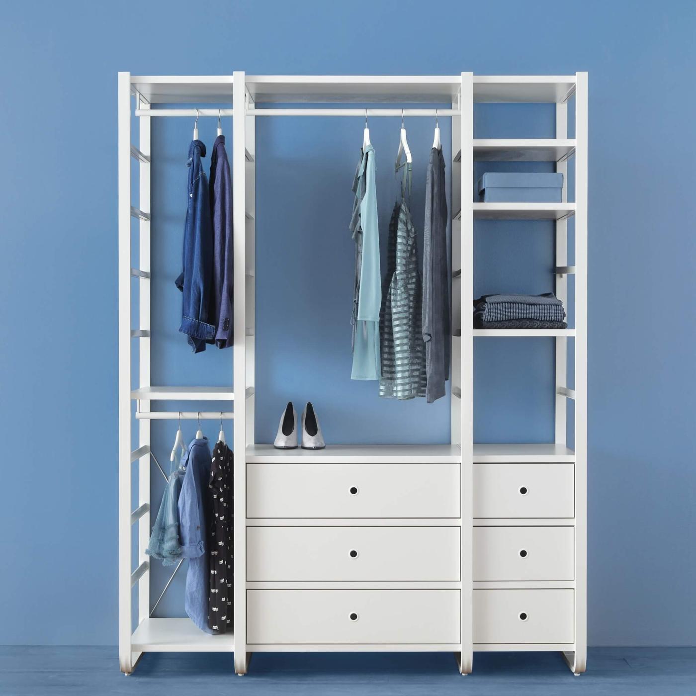An ELVARLI wardrobe combination stands in a blue room holding clothes hanging on a rail, bags and other items.