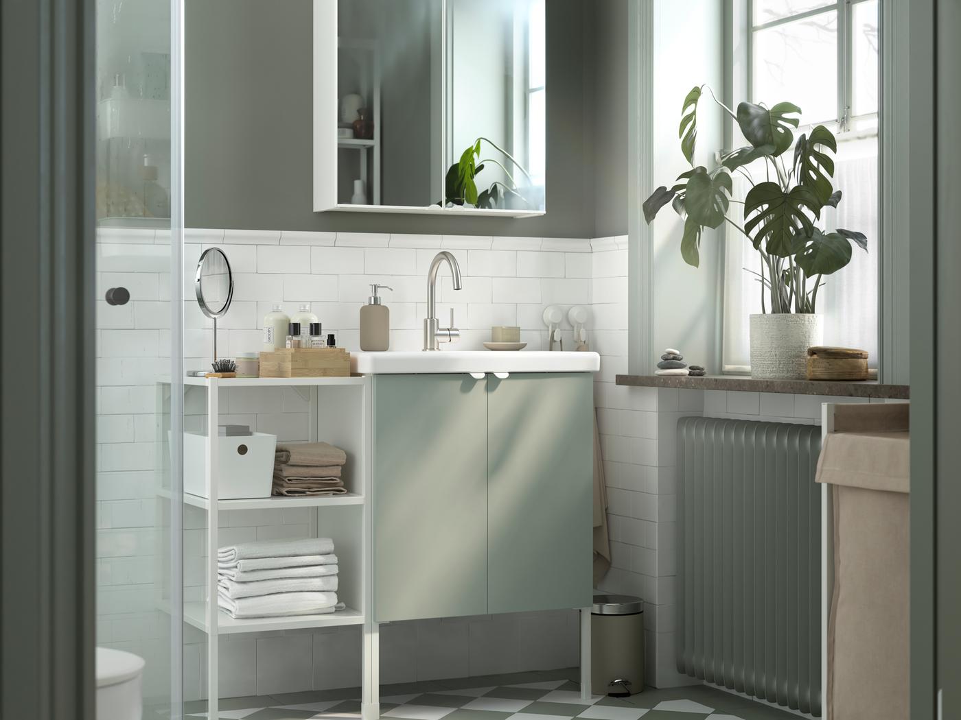 An ENHET cabinet in white with two doors and an open shelf to the left filled with towels, in a grey and white bathroom.