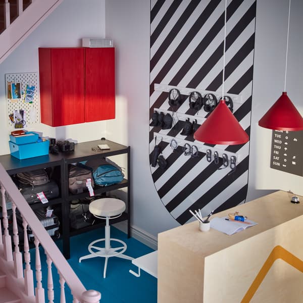 An entrance area with a reception desk in light wood, red lamps hanging above it and plenty of storage in the background.