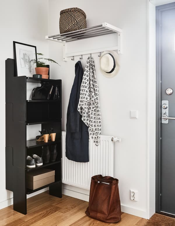An entrance is neatly arranged with a shelving unit, shelf, hooks, and only a few pieces of outerwear hung up.