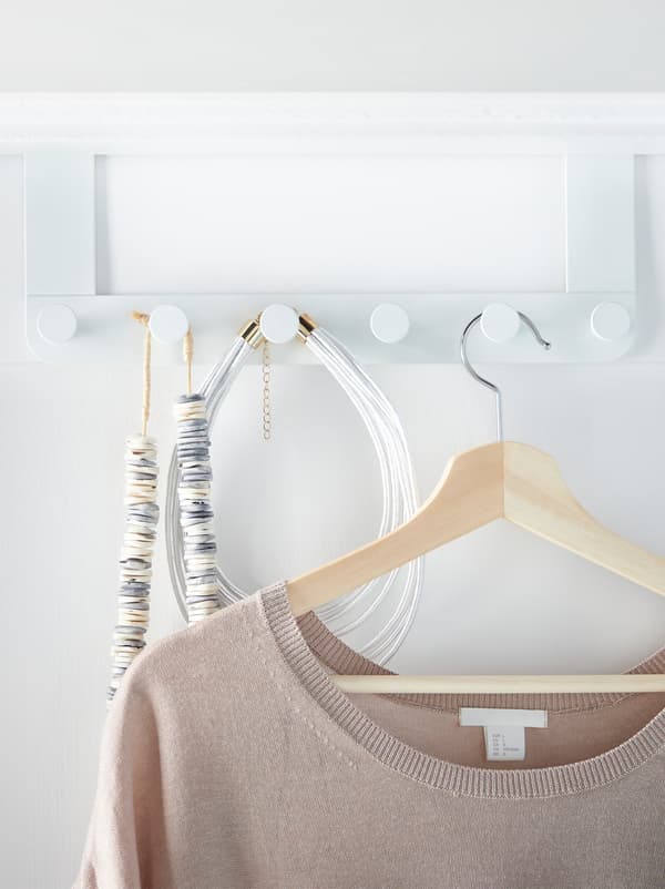 An ENUDDEN hanger with knobs placed over the the back of a door, with accessories and a top on a clothes hanger.