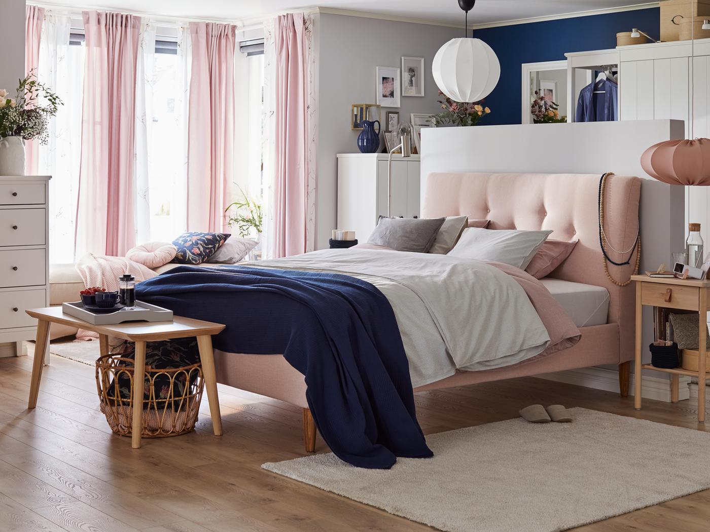 An IDANÄS upholstered bed with BERGPALM bed linen and a coffee table at its foot stands in the middle of a bright bedroom.