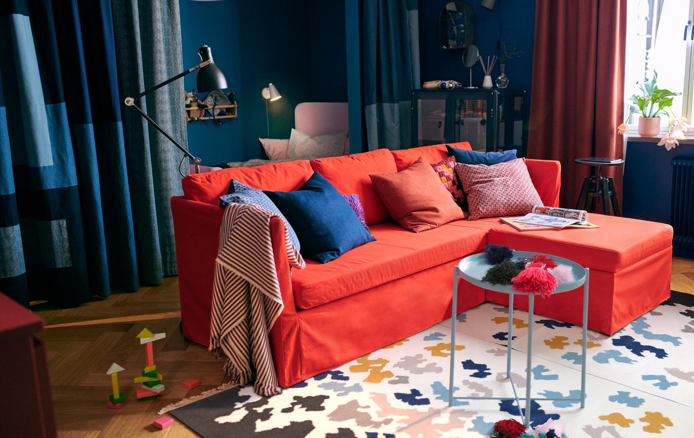 An IKEA BRÅTHULT red-orange sofa bed in a blue living room, with a patterned rug on the floor.