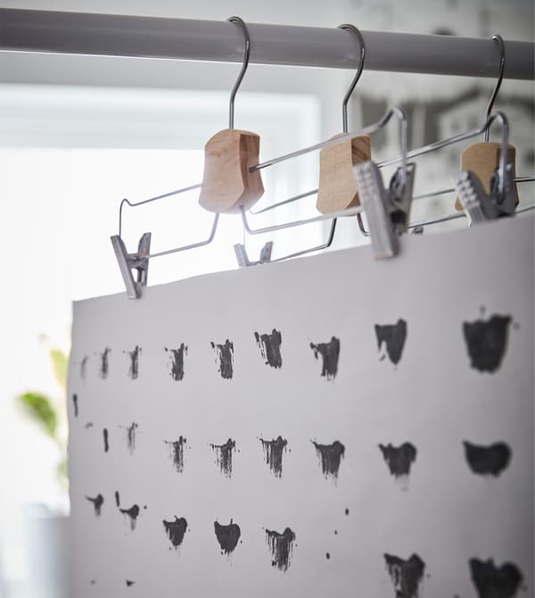 An IKEA BUMERANG trouser/skirt hanger displaying a black and white print for decoration in a dorm room.
