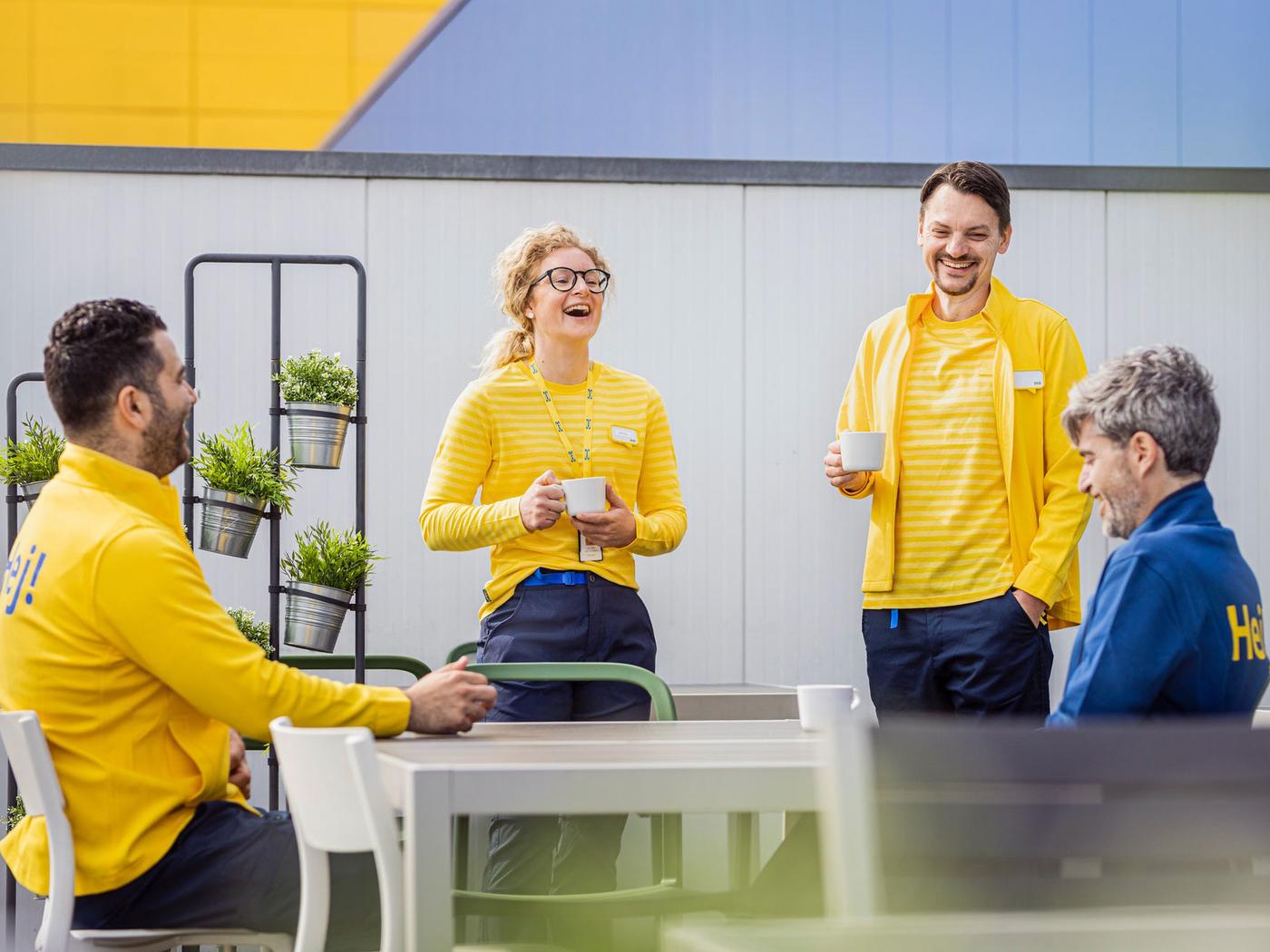 An IKEA co-worker dressed in a yellow uniform waving to a colleague in the staff canteen.