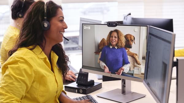 An IKEA co-worker has a headset on with a yellow shirt on and is speaking to a customer virtually on the computer.
