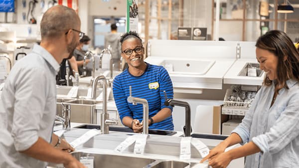  An IKEA co-worker in a blue shirt helping two customers in an IKEA store.