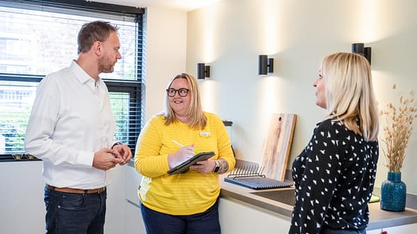 An IKEA co-worker in a yellow shirt assisting two customers in their home.
