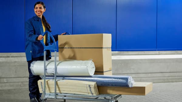 An IKEA co-worker pushes a trolley with IKEA packages and a rolled-up mattress in plastic.