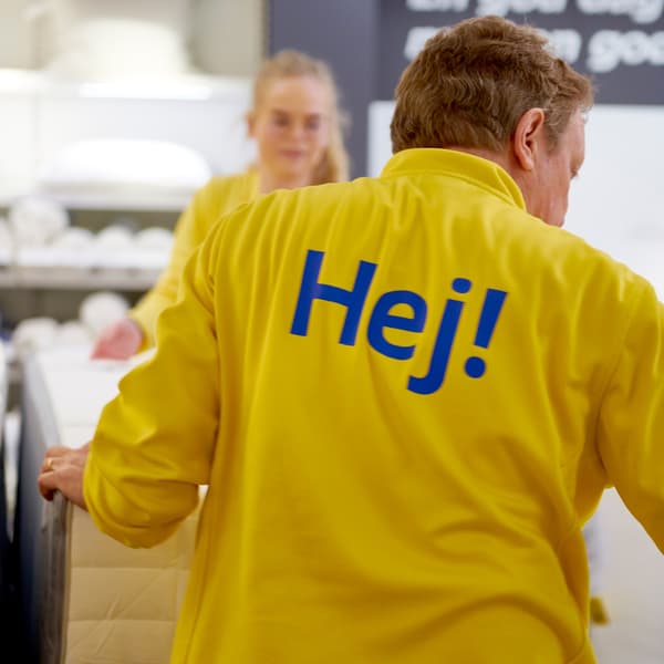 An IKEA co-worker wearing a yellow uniform with the word “Hej!” on the back of the shirt.