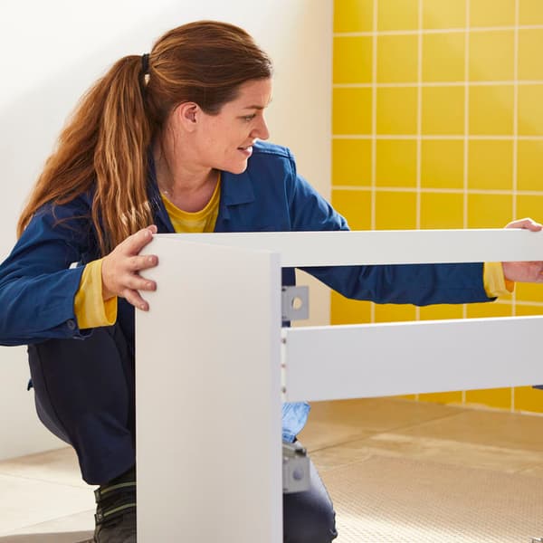 An IKEA coworker assembling a white storage unit.