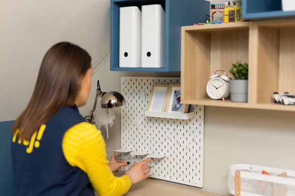 An IKEA designer arranging items at a child’s desk in a study area, adjusting accessories on a pegboard and shelves to create an organized and functional workspace.