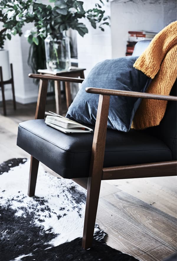 An IKEA EKENÄSET armchair, with a blue cushion and an orange jumper across the backrest.