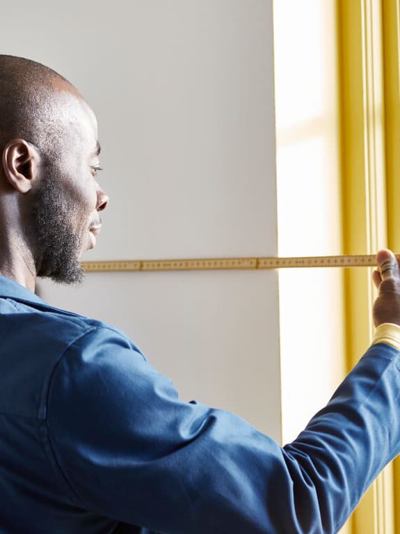 An IKEA employee measures a wall to hang curtains