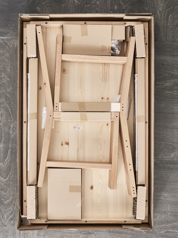 An IKEA flatpack with the top removed revealing a pine chair waiting to be assembled.